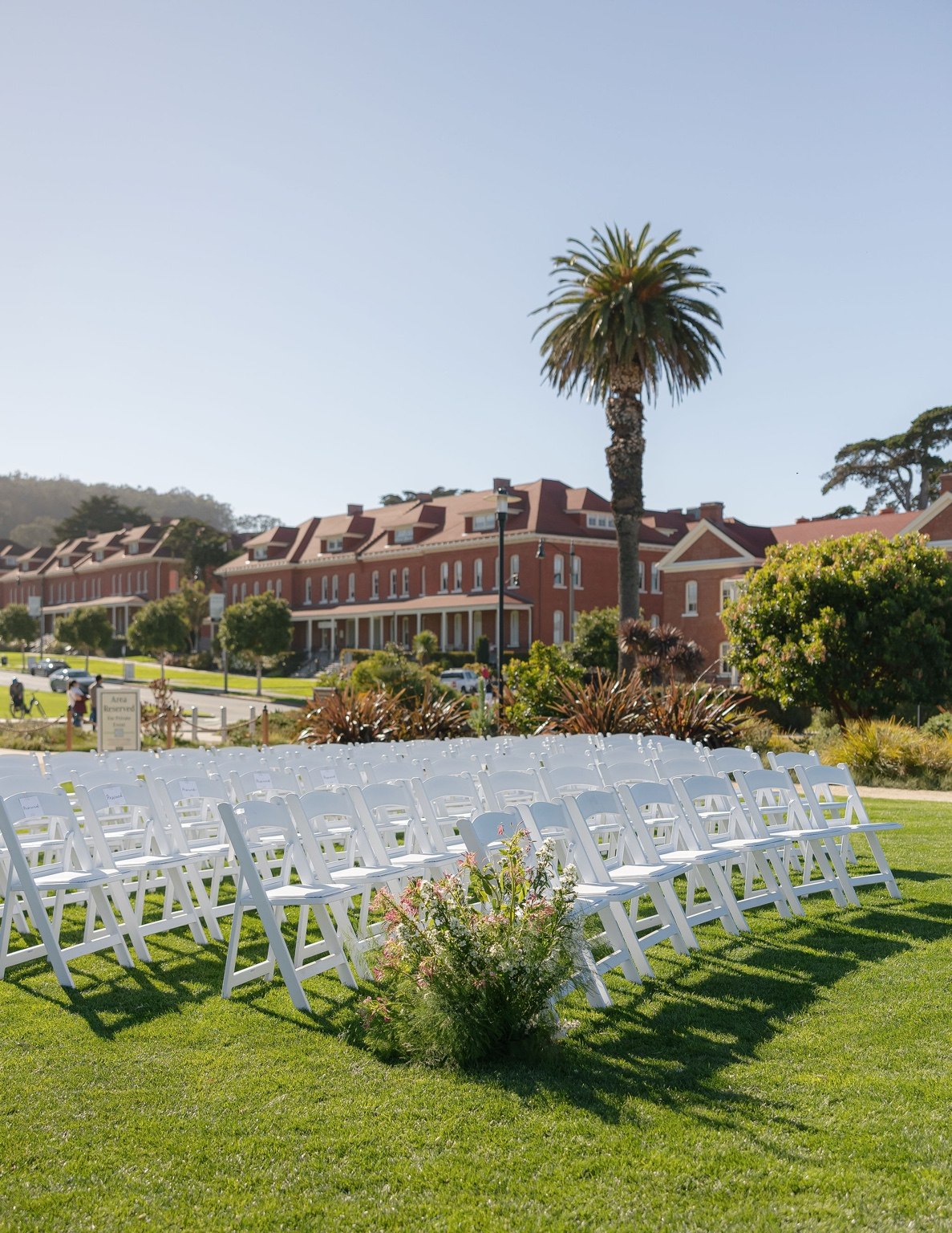 Rows of white chairs set on a lawn between brick buildings and palms for a garden ceremony
